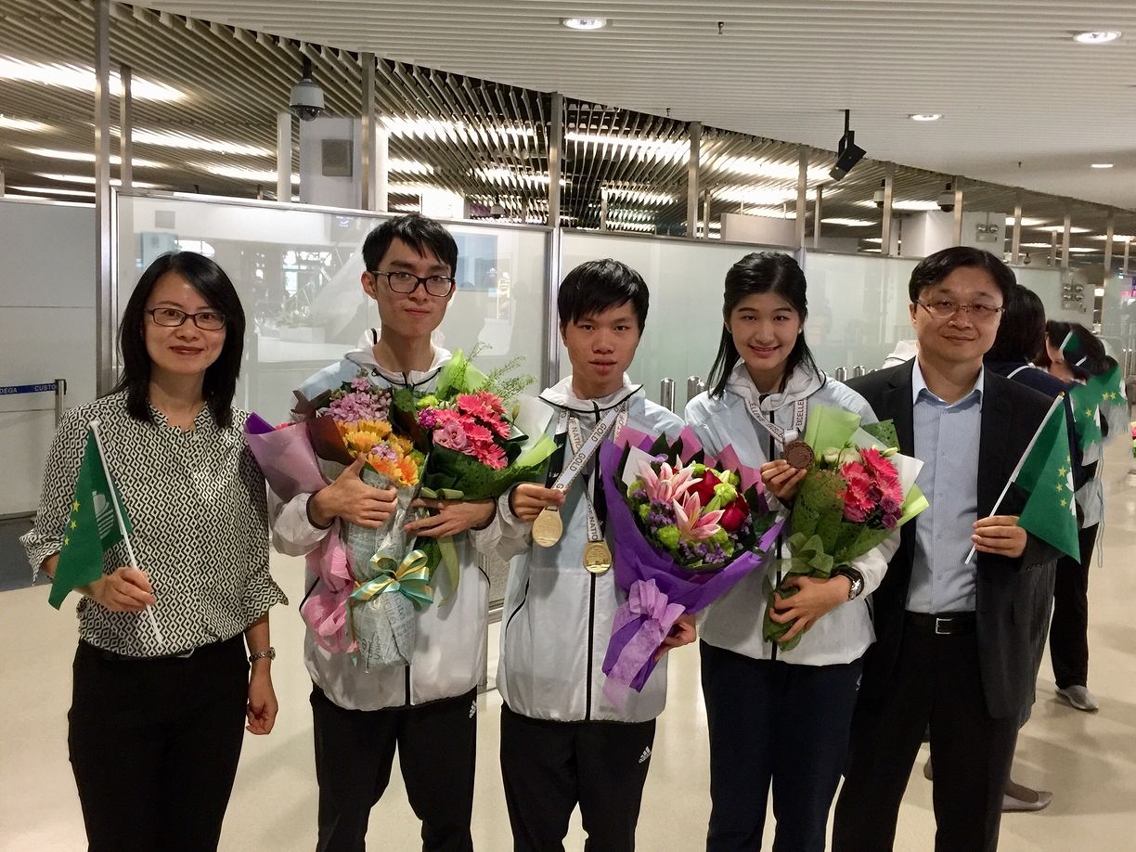 理工學生馮學健（中）及趙穎壯（右二）在競賽中勇奪金牌及卓越表演獎，學生事務處處長及電腦學課程主任迎接回澳