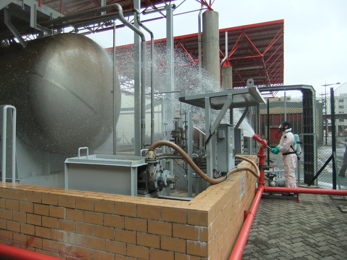 Um funcionário, vestido com o equipamento de protecção individual, a aspergir água no tanque de armazenamento com fuga de hidróxido de amónio, durante o exercício de simulação